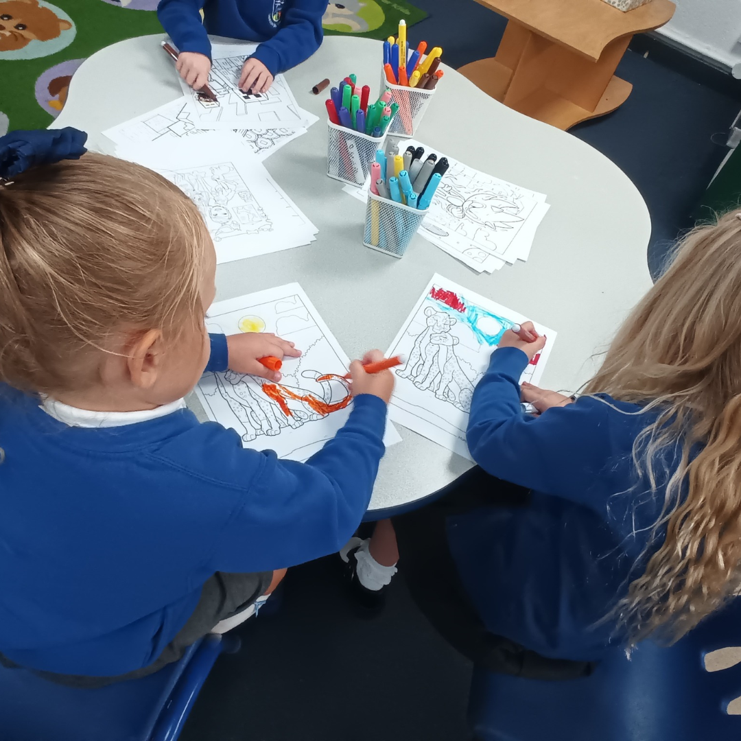 two girls in reception colouring at a table. They are wearing a blue school uniform